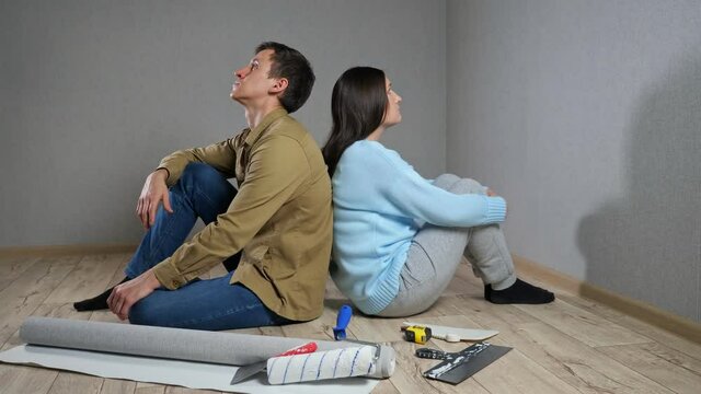 Young couple sits on parquet floor among building materials in room after quarrel because of renovations.