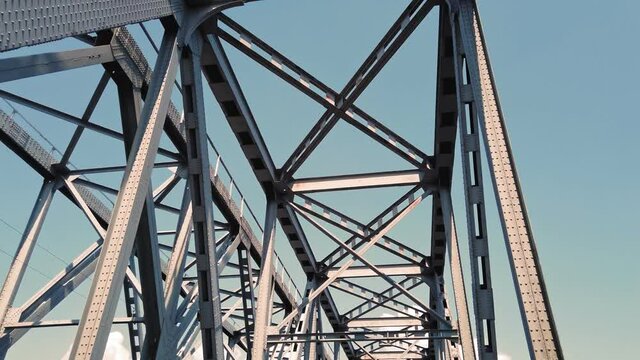 metal bridge. rough iron constructions against blue sky, filmed in motion from a car. bottom view. Railway and road bridge across the river. Silhouette of crossing steel beams.