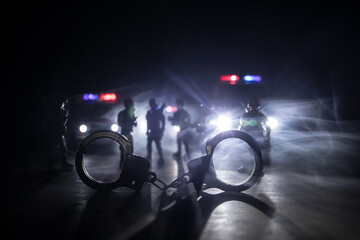 Police raid at night and you are under arrest concept. Silhouette of handcuffs with police car on...