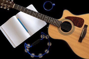 Acoustic guitar, tambourine, notepad and coffee cup on black background.