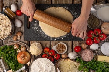 Many ingredients for making pizza, pie, ravioli, pasta. The cook rolls out the dough with a wooden rolling pin. A high angle view. Restaurant, hotel, pizzeria, home cooking, cooking blog.