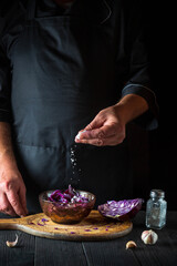 The chef sprinkles the salad with fresh red cabbage salt. Healthy food preparation in the restoran kitchen on a wooden table
