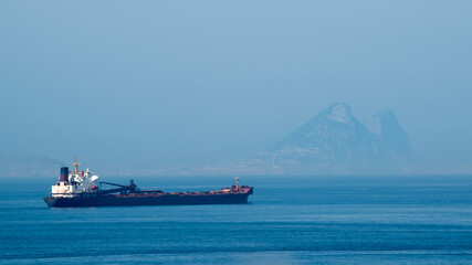 A freighter sails the Mediterranean Sea with the Rock of Gibraltar in the distance through the haze.