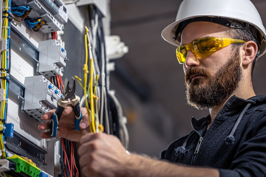 A male electrician works in a switchboard with an electrical connecting cable.