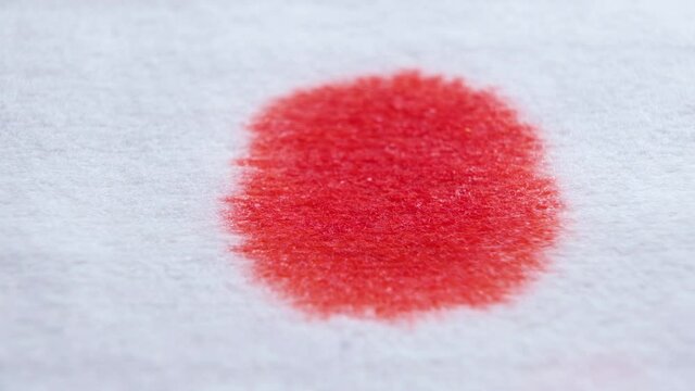 Red blood drops on a white bandage, paper or cloth-like surface. Splattering red color of blood, bloodstains reveal on white background. Shallow depth of field. Macro view.