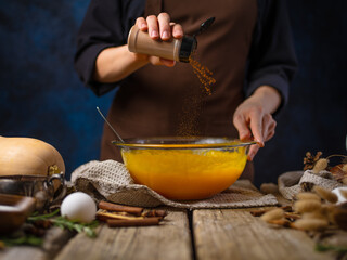 Bright orange pumpkin filling for American pumpkin pie in a large glass bowl. The cook adds spices to the filling. Levitation. Ingredients. Lots of objects. Decor. Wooden texture.
