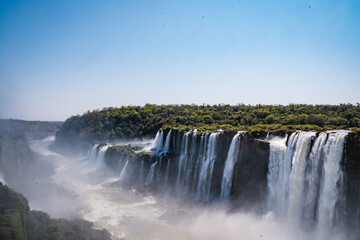 a waterfall in the middle of the forest with blue sky in the background.