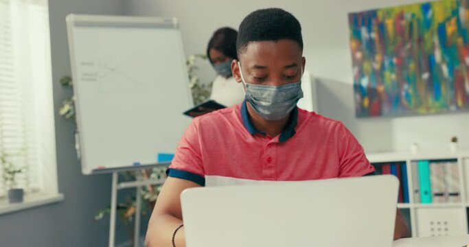 A busy woman stands at the blackboard holding a tablet, searches for the right graphic, prepares a diagram, a man sits at desk entering the data into the system needed to create the diagram