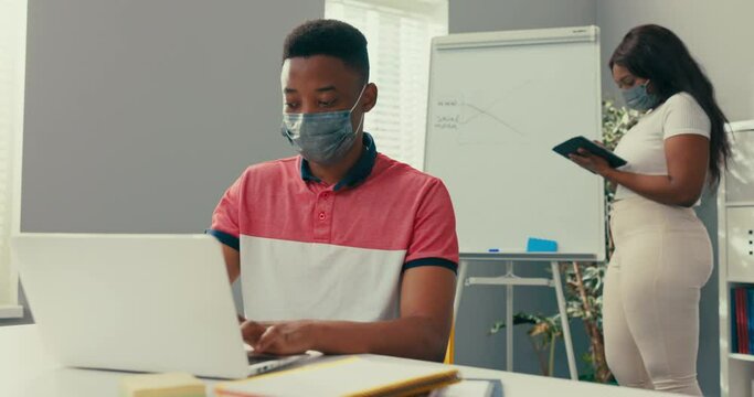 A busy woman stands at the blackboard holding a tablet, searches for the right graphic, prepares a diagram, a man sits at desk entering the data into the system needed to create the diagram