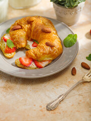 One fresh croissant with butter, fresh strawberries, mint leaves and almonds. Breakfast for one person. Food design, advertising, restaurant, hotel, confectionery, café, home cooking.