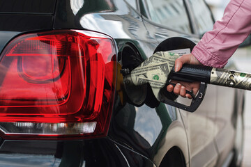 Woman's hand fuels the car. Girl at the gas station fills the tank with gasoline fuel. The rise in fuel prices, a concept idea. Filling gun and money dollar