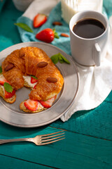 French croissant with fresh strawberries, mint leaves, almonds and a cup of fragrant coffee. Beautiful still life. Turquoise background. It's not like people. Advertising, café, restaurant, hotel.