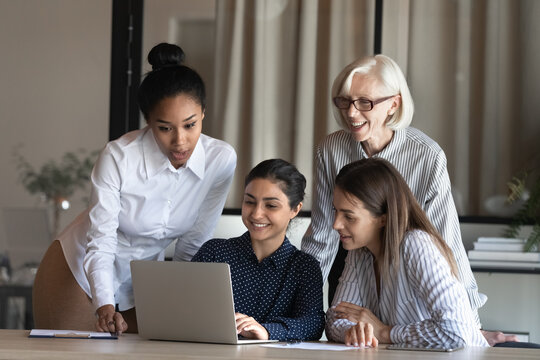 Smiling Indian Female Show Original Project Decision Easy Working Solution On Pc Screen To Multiethnic Women Colleagues Of Diverse Age. Successful Ethnic Lady Worker Share New Strategy With Teammates