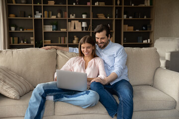 Happy young family couple using computer, shopping online, watching film, planning travel vacation booking tickets, communicating distantly in social network or web surfing, tech addiction concept.