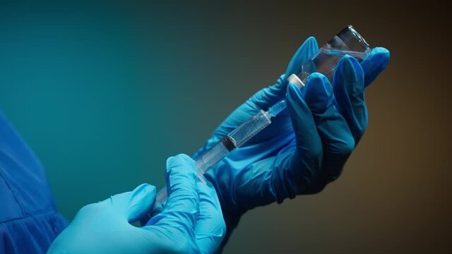 Doctor filling syringe with solution on blurred background. Nurse wearing protective gloves showing sample of medicine, vaccination against covid-19, laboratory research concept. Coronavirus vaccine.