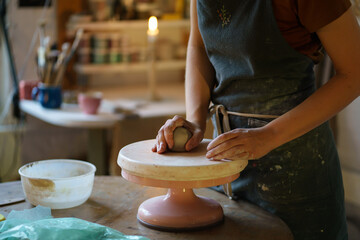 Sculpturing from raw clay on wheel: female artist hands using tool for shaping and creating pottery in studio. Woman owner of ceramics workshop at workplace. Craftsmanship hobby or business occupation