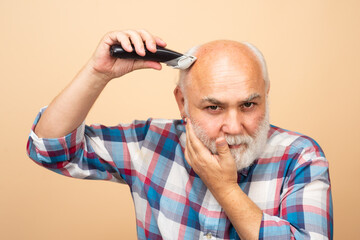 Portrait of mature man being trimmed with hair clipper in barbershop, haircut with an electric...