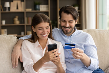 Happy bonding young family couple entering payment information from credit bank card in mobile...