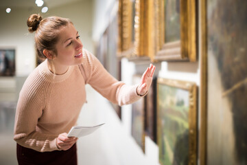 Portrait of young woman visitor with guide book looking at exhibition in art museum