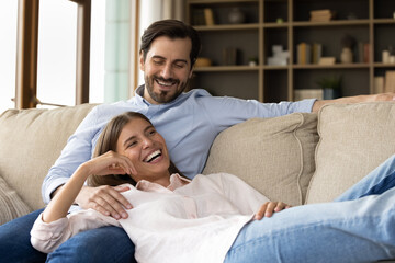 Happy bonding loving laughing young 30s family couple relaxing on comfortable couch in modern...