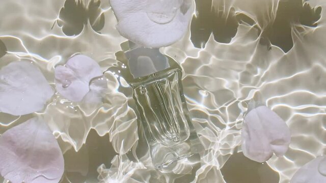 Glass perfume bottle, Cosmetic of aromatic essential oil. Top view slow motion of waves water. Clear water with reflections, refraction sunlight and shadows. Natural cosmetics and skin care. 4k 