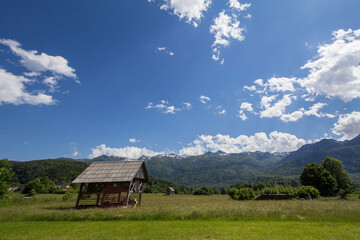 Typical agricultural landscape with a wooden barn in a middle of a field with a grass pasture meadow in Bohinj, Slovenia, in front of the Julian Alps. it is a landmark of slovenian rural activity. ..
