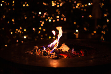 close up of fireplace with burning fire wood in cold winter night and bokeh christmas lights on traditional christmas market at Merano, South Tyrol, Italy - obrazy, fototapety, plakaty