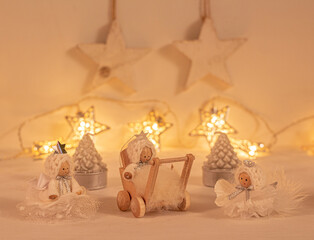 christmas festive scenery showing 3 handcrafted german Angel ornaments in warm golden light; front view with blurred bokeh star lights background on white wooden table