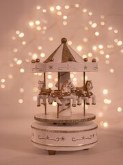 christmas festive scenery showing a musical box with golden carousel horses; front view with blurred bokeh lights background on white wooden table