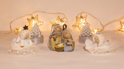 christmas festive scenery showing the Holy Family with 2 handcrafted angel ornaments in warm golden light; front view with blurred bokeh star lights background on white wooden table
