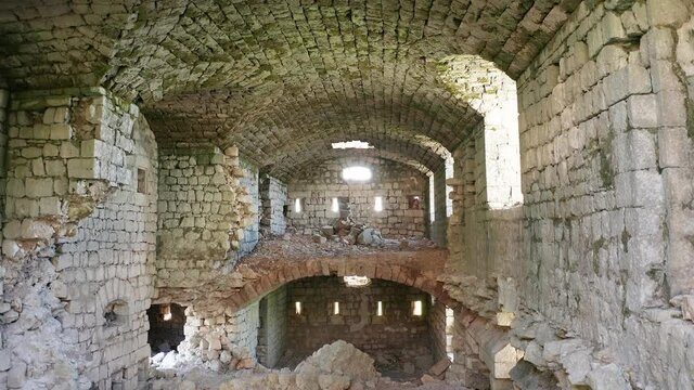 Medieval castle interior - ruin of old derelict stone fortress with partially collapsed walls and arched ceiling, light entering through windows and slits. Fort Kosmac in Montenegro, Europe.
