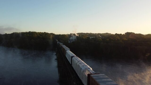 Aerial follow footage of freight train traversing elevated bridge over Catawba River in South Carolina, USA. Rising shot.