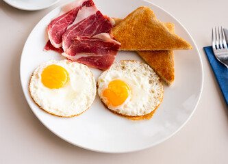 Fried eggs served on plate with bacon and toasts, breakfast meal