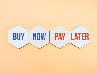 Wooden hexagon with text buy now pay later against dark yellow background.