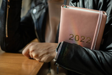 Inspired young woman with a smile looking through window and holding coral colored diary 2022