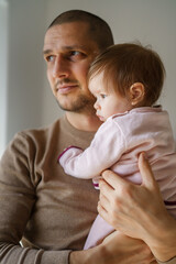Caucasian man holding his baby girl child daughter by the window at home in room in day - parenthood care father's day concept real people