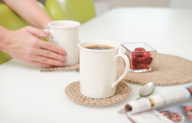 woman serving a coffee in a white light kitchen using eco knit jute tablemats. good morning concept. crop view.