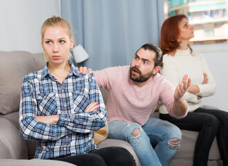 Upset girl sitting after quarrel and man with mother on background at home