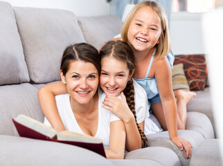 Portrait of happy single mother laying on sofa with two daughters at home
