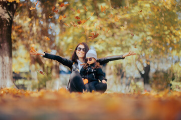 Happy Mother Throwing Leaves Holding her Daughter in the Park