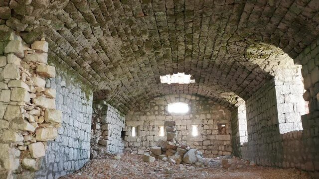 Medieval castle interior - ruin of old derelict stone fortress with partially collapsed walls and arched ceiling, light entering through windows and slits. Fort Kosmac in Montenegro, Europe.