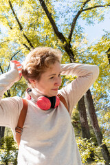 Portrait of adult woman who listening to music in wireless headphones. Walk in the park.