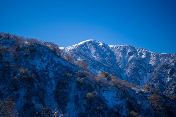 富山県上市町にある雪が積もった晩秋のクズバ山の登山道から剣岳、大日岳、猫又山などを見る風景 A view of Mt. Kuzuba with snow on the trail in late autumn in Kamiichi Town, Toyama Prefecture, looking at Mt.Tsurugi, Mount Dainichi.