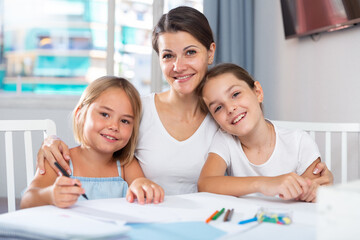 Portrait of happy mother with two daughters draw at table at home