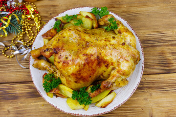 Baked whole chicken with potato and Christmas decorations on a wooden table. Top view