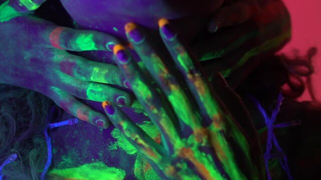 Close up on hands with Neon Halloween make up glowing under neon lights.