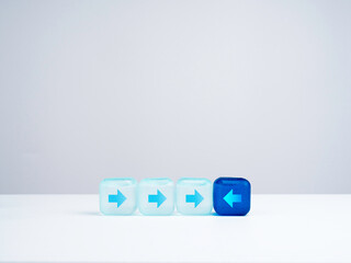 Leadership, unique, thinking differently, individual and standing out from the crowd concept. Blue cube block with arrow facing the opposite direction of light blue cube blocks on white background.