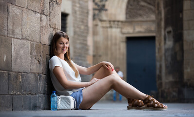 Fototapeta na wymiar Smiling young woman sitting near old stone cathedral wall