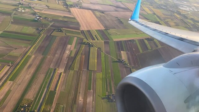 Close up shot of turbine of airplane and rural colorful farm fields in with differenet pattern during landing approach