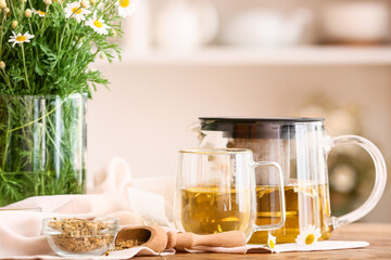 Teapot and cup of tasty chamomile tea with flowers on table